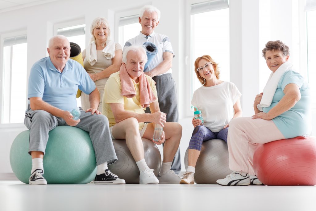 A group of older adults smiling while finishing an exercise routine. Falls in the  elderly risk factors and preventions.