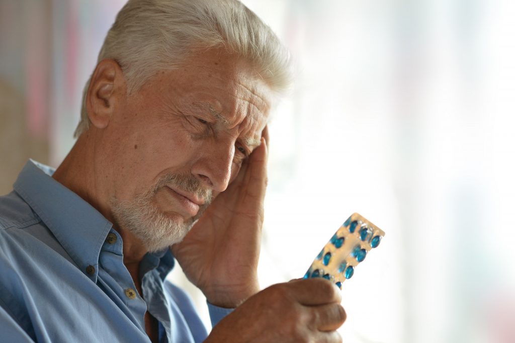 Caucasian man holding medications in his hand. Falls in the elderly risk factors and prevention.