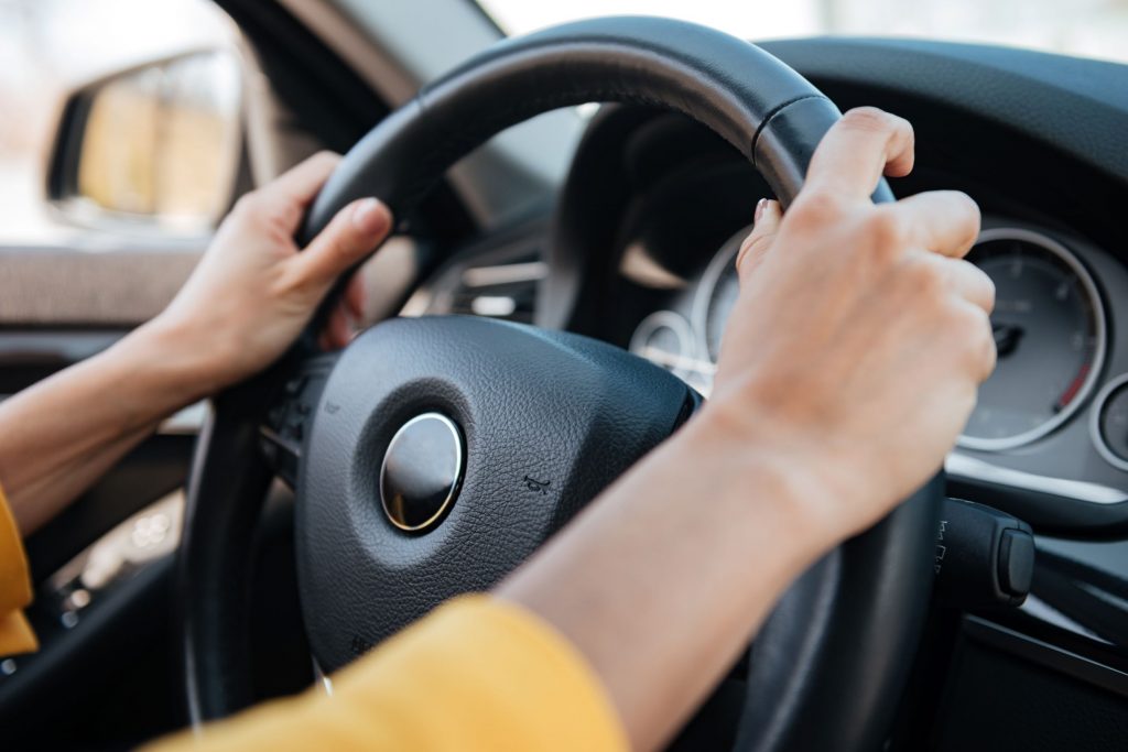 Picture of the arms of a female with both hands on the steering wheel of a car. Home health care jobs. 