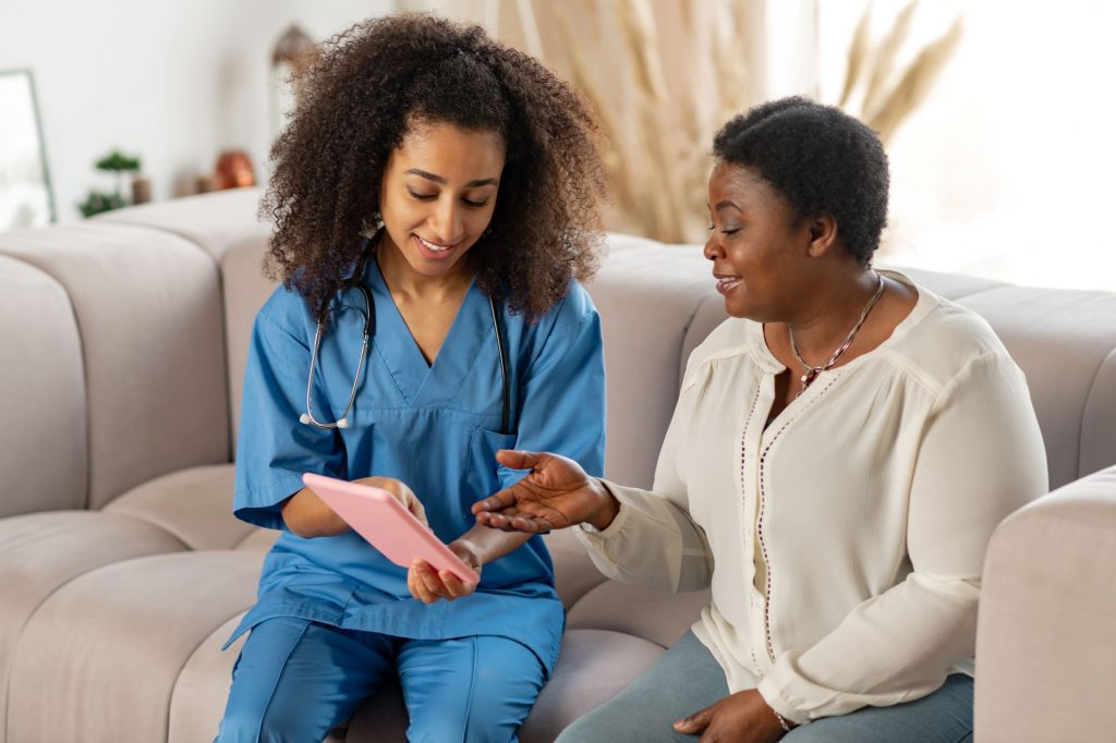 Young African American female nurse, physical therapist, occupational therapist treating patient while at home. Home health care jobs.