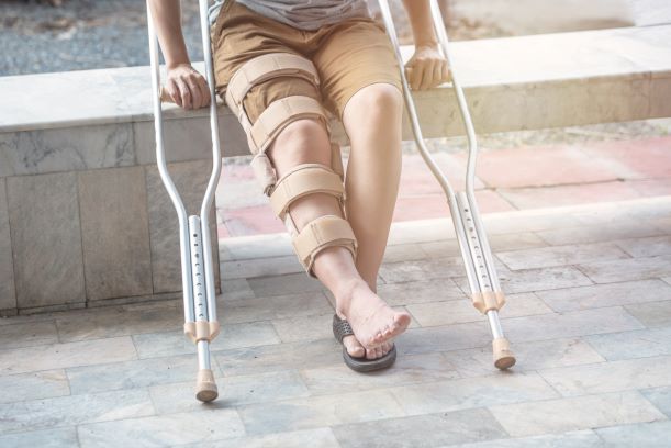 A picture of a woman sitting with a leg brace and bilateral axillary crutches in hand.