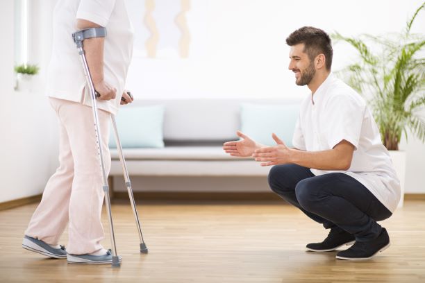 A picture of a woman using forearm/lofstrand crutches and a doctor/therapist kneeling in front giving instructions. 