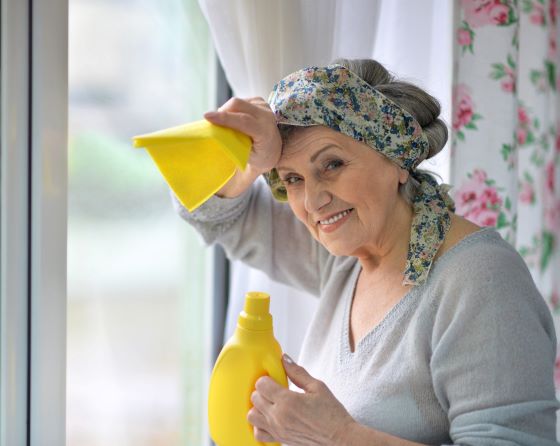 Older caucasian adult woman with rag and cleaning agent in hand, cleaning the windows. Exercise for seniors at home.