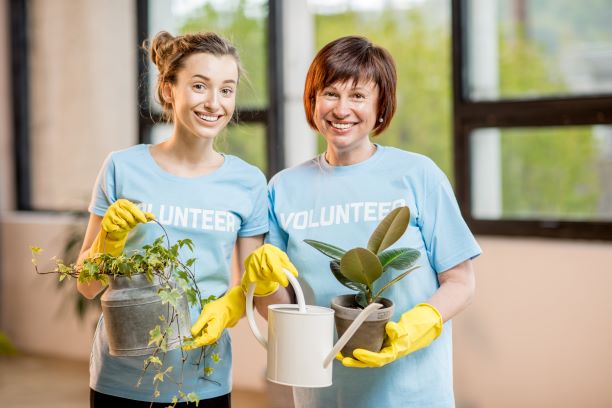 Younger and older caucasian women holding plants with volunteer shirts on. Exercise for senior citizens.