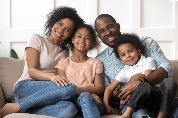 African American Family smiling wile stting on a couch. Used to display CARES ACT benefits for families/individuals.