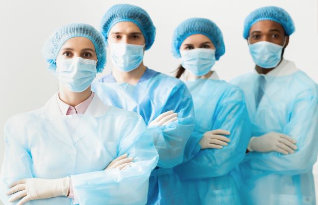 Multiple male and female hospital workers standing with gowns, masks, and gloves.
