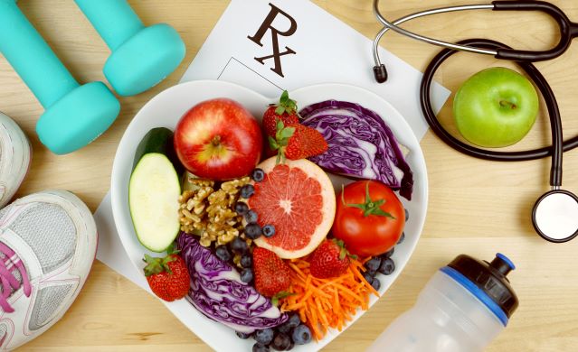 Image of a bowl of healthy food sitting on top of an RX paper with weights, shoes, water bottle, and stethoscope around it. 