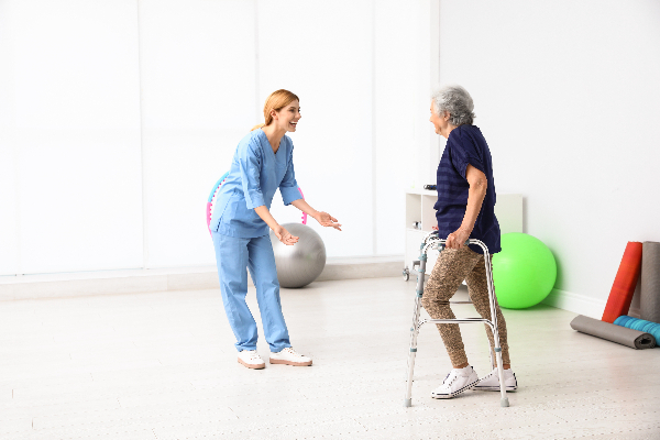 Older woman walking toward female therapist using rolling walker demonstrating weight-bearing precautions