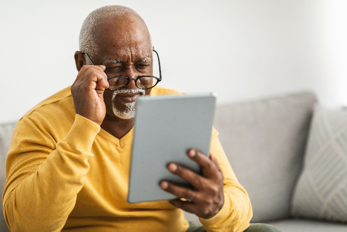 African American man reading a tablet with glasses in hand.