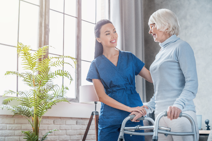 Physical therapist helping older woman to walk with a walker