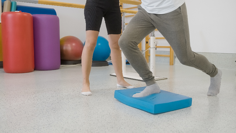 Caucasian man standing on balance pad with physiotherapist